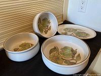 Four Denby Troubadour stoneware serving dishes arranged on a black surface: one oval platter, one large bowl, two smaller bowls, each with cream base and floral green and brown interior pattern.