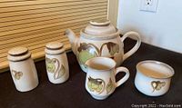 Full set depicting teapot, creamer, sugar bowl, salt and pepper shakers on black surface