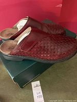 Clarks wine colored slip-on shoes resting on their box, showing woven leather upper design.