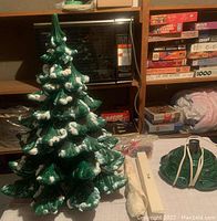 Full view of the assembled green ceramic Christmas tree with snow accents next to star topper and miscellaneous items on shelves behind.