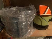 Photo of large stainless steel stock pot wrapped in clear plastic bag alongside JC Penney slow cooker on wooden surface.