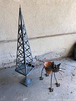 Photo showing the metal garden obelisk and metal cat plant holder together from a distance on a floor against a wall.