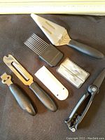 Photo displaying the full set of Pampered Chef utensils including pie lifter, tomato cutter holder, scraper, cheese slicer, zester, and scissors with covers on a black background.
