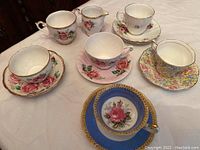 Top view showing full set of 6 teacups with saucers and cream and sugar set on a table with floral patterns and gold trim.