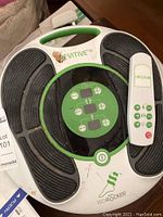 Top view of the Revitive Circulation Booster device showing the circular control panel and footpads, with remote control resting on the unit.