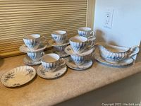 Set of tea cups stacked on matching saucers, small plate, and gravy boat on a counter showing floral Snow White Regency pattern