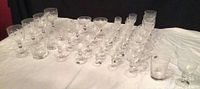 Full view of complete assortment of clear etched Stewart Crystal stemware on white cloth, showing various sizes and glass shapes.