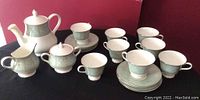 Full set including teapot, creamer, sugar bowl, 8 cups, and 8 saucers arranged on a surface with red background