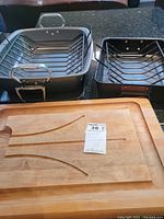 Overview of the three items: wooden cutting board with Circulon and All-Clad pans with racks placed on top, all shown needing cleaning.