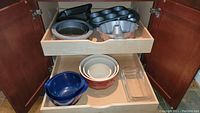 Full view inside cabinet showing all bakeware items including mixing bowls, loaf pans, muffin tin, bundt pan, pie pan, and glass loaf dish.