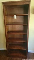 Front view of one wood bookcase with five shelves visible, medium brown finish and some wear marks.
