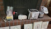 Photo shows entire lot of five kitchen appliances arranged on brick mantel: food processor, coffee grinder, hand mixer, toaster, and popcorn popper.