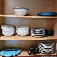 Cabinet shelves with all plates, bowls, and mugs stacked and grouped by brand and style