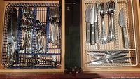 Top view of two drawers containing flatware sets - knives, forks, spoons separated into different sections in plastic trays.