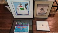 Four framed prints laid on floor including a cat print holding a green fish, Noah's Ark print, and two colorful prints.