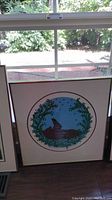 Framed art of an otter in water surrounded by leafy branches shown by window light