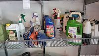 Shelf containing assorted gardening chemical bottles and pairs of gloves, various labels for slug and snail bait, rose disease control, and fertilizer visible.