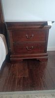 Front view of a Bassett nightstand showing two drawers with metal handles, distressed dark wood finish, classic molding details on top and base.