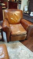 Front view of tan leather recliner showing worn seat cushion and scratches on arms.