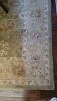 Full view of the rug showing floral and vine border design in beige and green tones with burgundy accents.