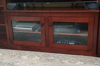 Front view of dark wood TV stand with glass doors showing electronic devices inside and black round knobs on doors.