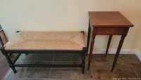 Wooden side table and woven bench set placed against wall, view shows the bench seat and table base
