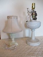 Photo showing both ceramic lamps side by side. One lamp has no shade and a taller ribbed base; the other has a scalloped fabric lampshade on a shorter base.