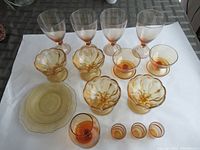 Full view of all amber glassware items including stems glasses, footed dessert dishes, tumblers, and pedestal bowls arranged on a white sheet.