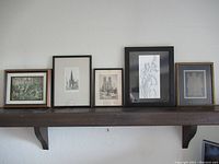Wide shot of five framed art prints displayed on wall shelf, showing various sizes and frame styles.