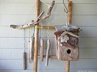 View of rustic driftwood bird house attached above the garden wind chime made of driftwood pieces hanging from a horizontal branch.