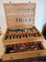 Open wooden box showing brass cutlery assortment inside drawers and compartments