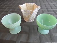 Three items on table showing ceramic vase center and two green patterned glass goblets flanking it