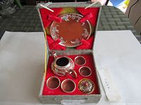 Full view of tea set inside box showing teapot, four teacups, larger container, and decorative plate inside patterned box.