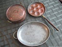 Overhead photo of the complete cookware set on a checkered surface including the lidded pot, round indentation pan, and oval pan.