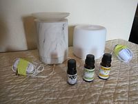 Two essential oil diffusers and three bottles of essential oils on a quilted surface.