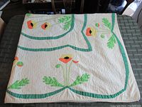 Quilt folded in quarters showing full appliqué flower pattern and green borders on white background.
