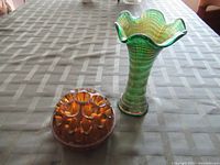 Photo showing full views of green glass vase and amber glass flower frog on tablecloth.