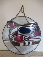 Full view of circular stained glass wall-hanging with attached hanging chain, showing colored glass sections and metal framing.