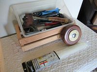 Full view of the plastic container holding various tools including a vintage hatchet, next to a wooden framed round barometer placed on a surface.