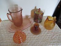 Photo showing the entire lot of six items including pitcher, platter, two lidded jars, creamer pitcher, and candlestick on quilted surface