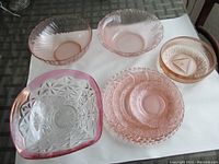 Overview of six pink glass dishes on table showing variety of bowl and plate shapes and patterns.