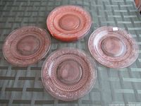 Set of seven round pink glass plates with embossed floral and geometric patterns, some stacked and spread on a surface.