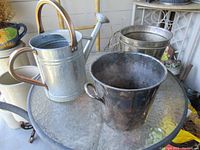 Photo showing two garden buckets and a watering can on a glass table.