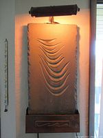 Full view of ceramic art panel with light lit, showing carved wave design and metal base with embossed pattern.