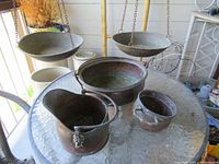 Photo of three copper pots and two hanging balance scale dishes displayed on a glass table.