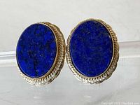 Front view of the pair of oval lapis lazuli earrings showcasing the deep blue stones with gold flecks and gold and seed pearl settings.