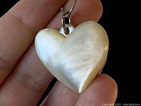 Close-up view of the heart pendant held on a hand showing the natural surface and carved heart shape of the mother of pearl.