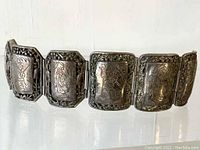 Full view of the bracelet displayed upright showing six linked octagonal panels with distinctive figurative engravings and decorative edges.