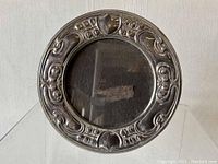 Front view of the ornate round sterling silver Art Nouveau picture frame with floral and scroll embossed decoration and glass insert.