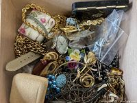 Full view of assorted gold-tone chains, wristwatch, floral blue carved brooch, and various jewelry and trinkets in box